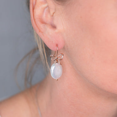 Close-up of an earring with a 18ct rose gold bow and luminous white pearl on 18ct rose gold 925 sterling silver hook back.