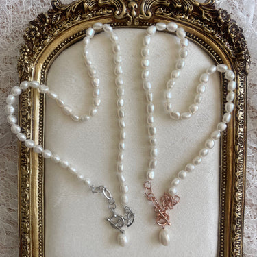 Two pearl necklaces, one rose gold and one sterling silver with toggle clasps in a decorative gold frame on a textured white background