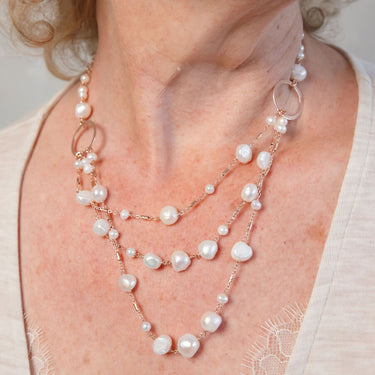 A triple strand necklace featuring white pearls and gold circle links 